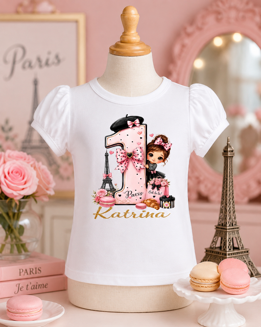 White t-shirt with a design of a girl, number 1, and Eiffel Tower on a mannequin against a pink-themed background.